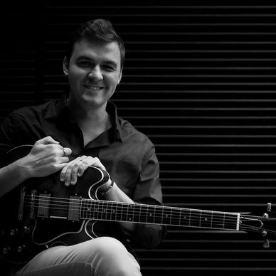 Young man smiling with an electric guitar in black and white.