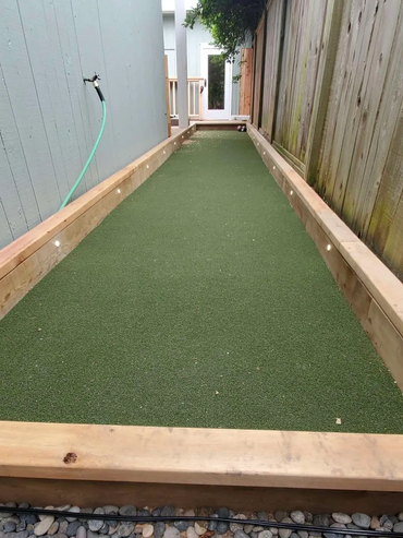 A backyard bocce ball court beside a house fence.