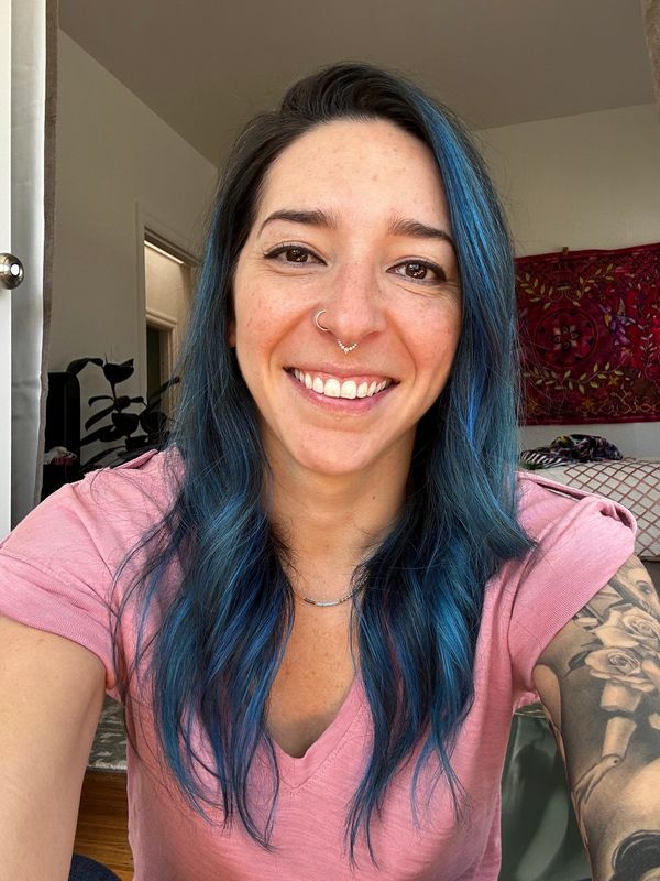 Smiling woman with blue hair and tattoos taking a selfie.
