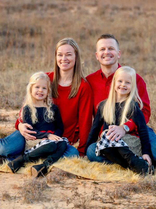 Smiling family of four sitting outdoors on a blanket in casual autumn attire.