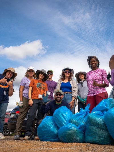 A group of volunteers posing with collected trash bags outdoors.