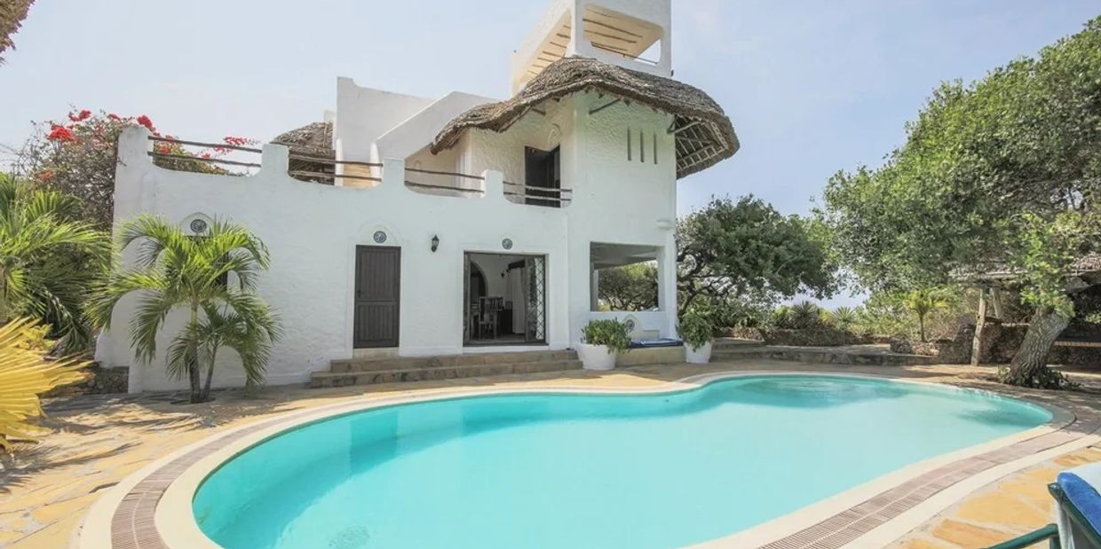 White Mediterranean-style house with a pool and lush greenery.