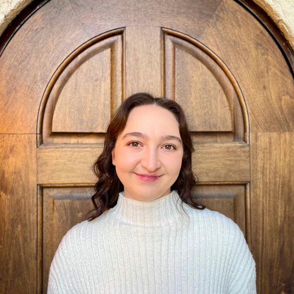 Young woman smiling in front of a wooden arched door.