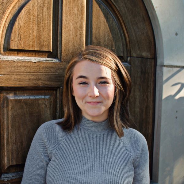 Young woman smiling in front of a wooden door.