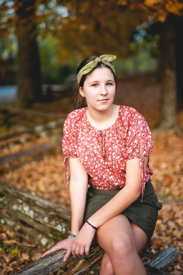 Young woman sitting on a wooden fence in autumn.