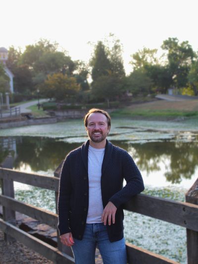 Man standing by a wooden fence near a pond.