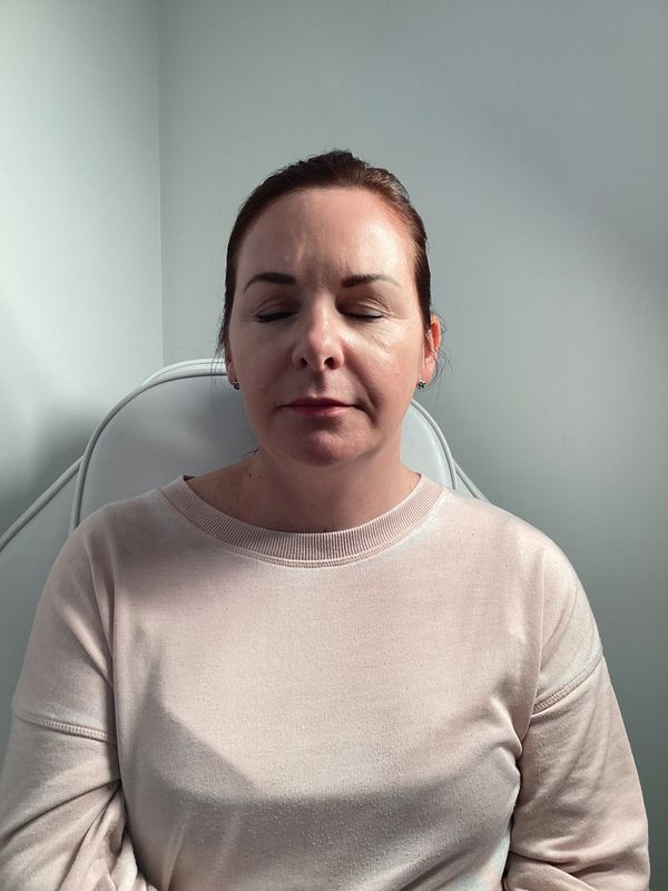 Woman with closed eyes sitting calmly in a light-colored room.