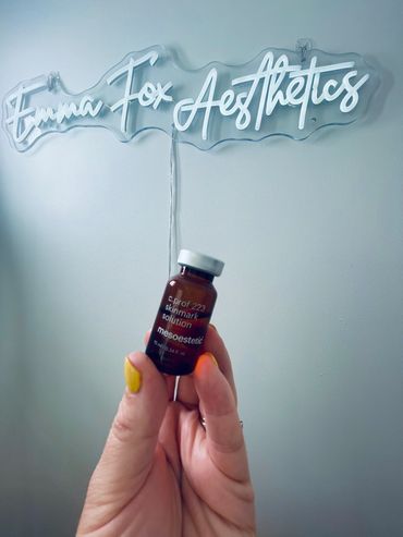 Hand holding a small vial in front of a neon sign saying Emma Fox Aesthetics.