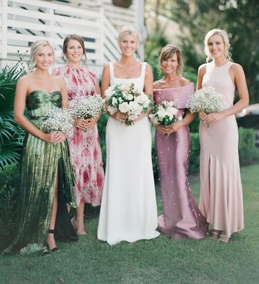 Five women dressed elegantly, posing outdoors with bouquets.