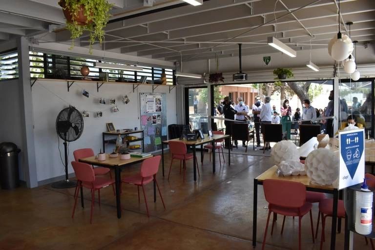 People gather outside a spacious indoor seating area with tables and chairs.