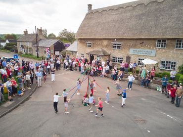 Children dancing around a maypole in a village street.