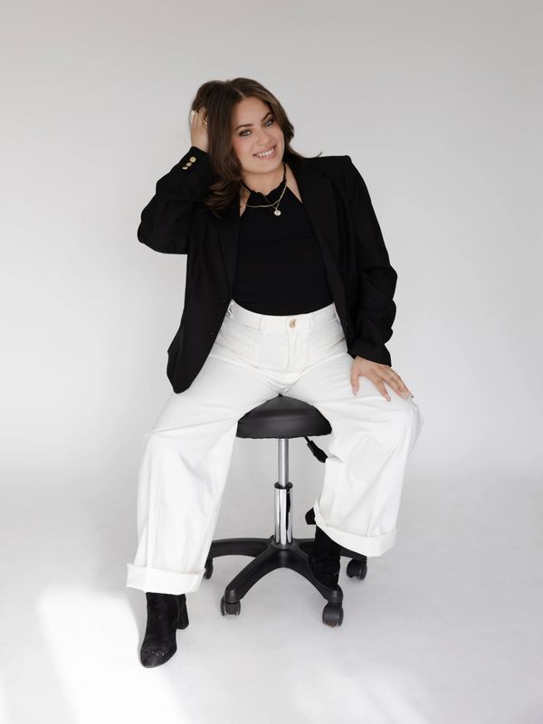 Young woman smiling, sitting on a chair, wearing black and white outfit.