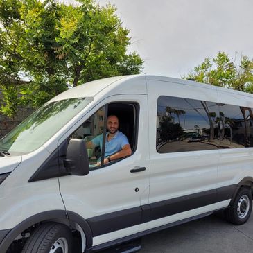 Man sitting inside a white passenger van, smiling at the camera.