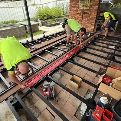 Three workers installing decking boards on a metal frame outdoors.