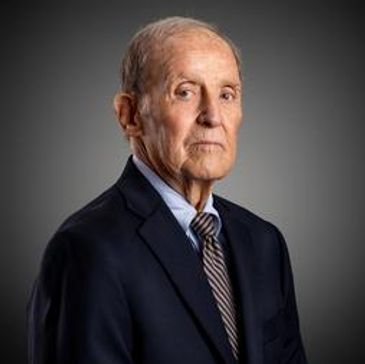 Elderly man in a suit posing against a gray background.