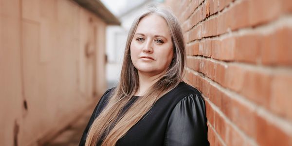 Serious woman stands by brick wall.