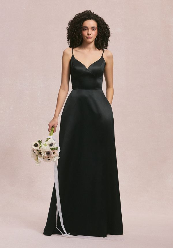 Woman in elegant black spaghetti strap gown holding flowers.