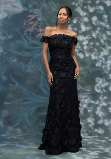 Woman in elegant black off-shoulder dress posed against artistic backdrop.