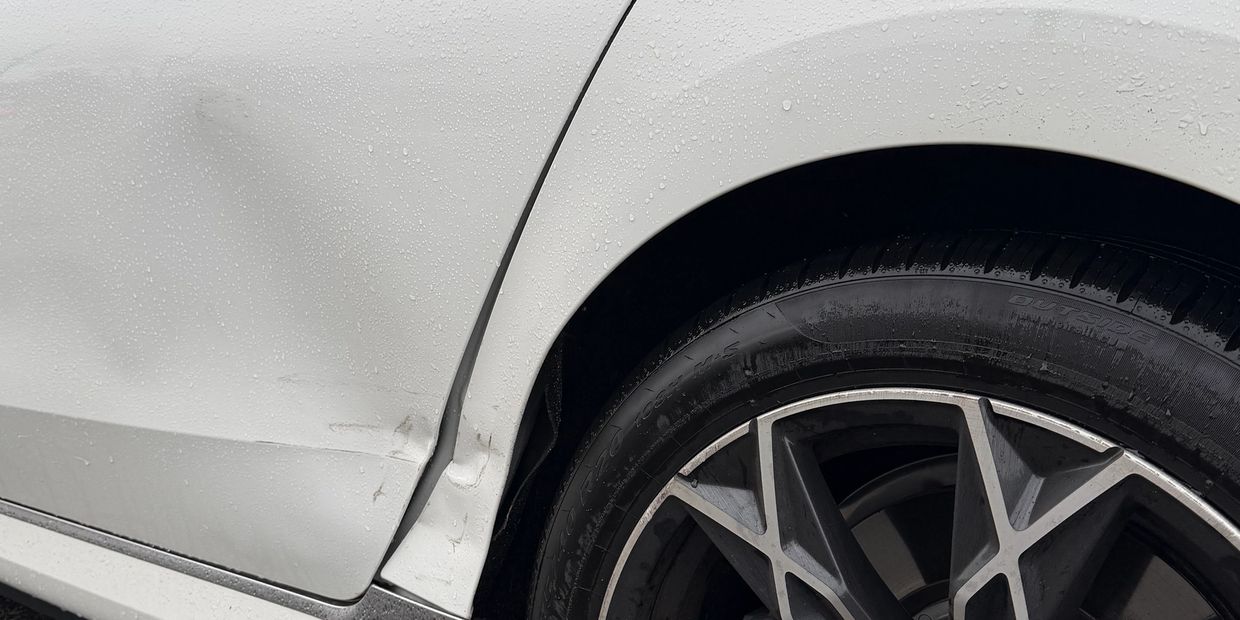 Close-up of a white car's dented rear wheel arch.