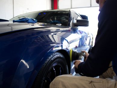 A man in an auto detailing shop near Johnson City, TN polishing the paint of a blue mustang.