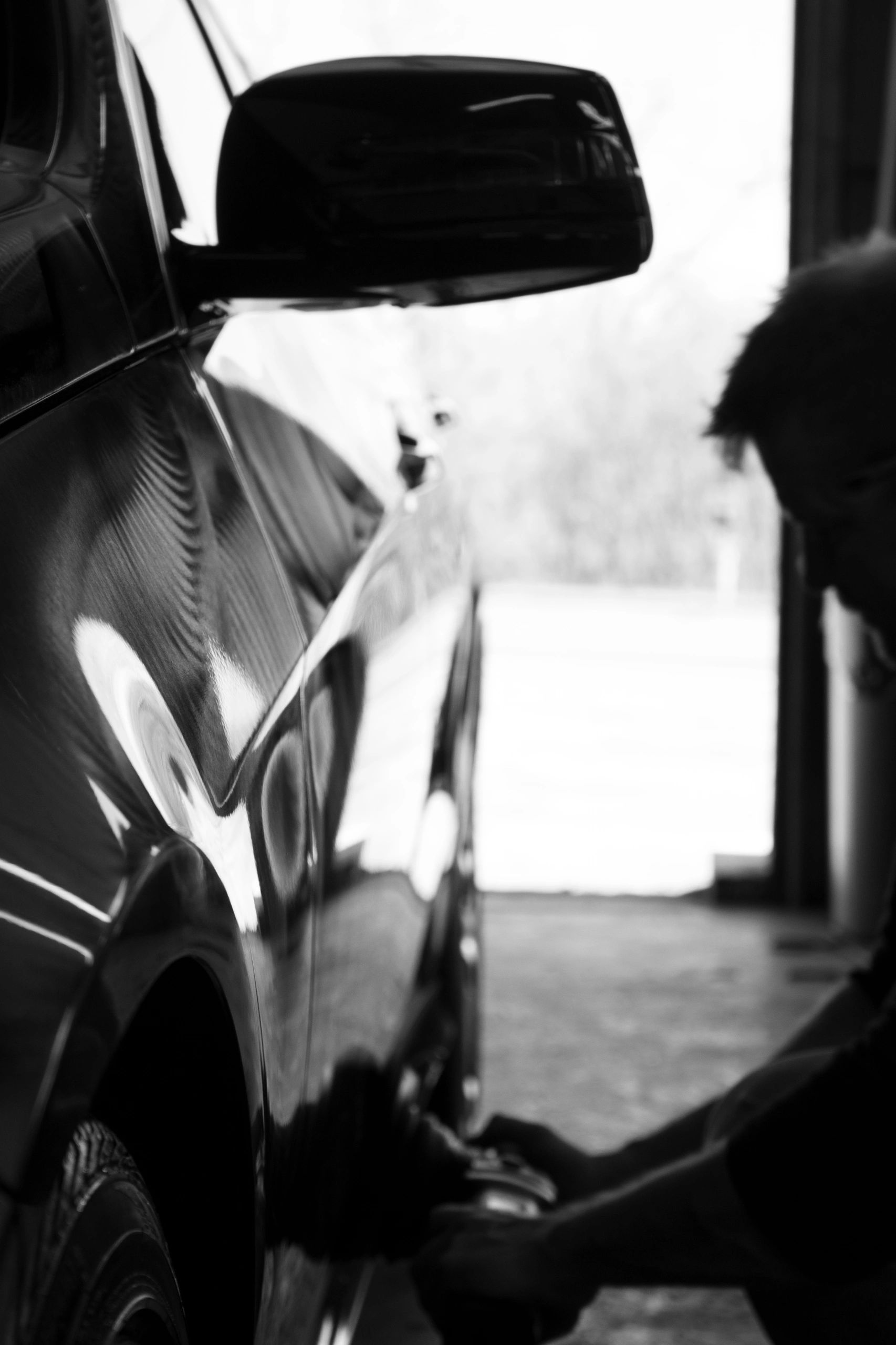 A black and white artistic photo of a man buffing a car with an electric buffer.