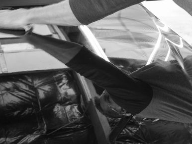 A black and white photo of a man reflected in the hood of a black BMW in an auto detailing shop.