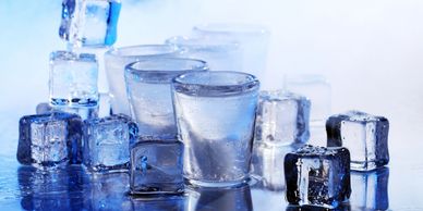 Ice cubes and glasses with water on a reflective surface.