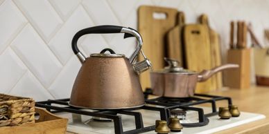 Copper kettle and saucepan on a gas stove with wooden cutting boards in the background.