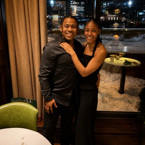 A happy couple dressed elegantly, smiling and embracing indoors with a snowy outdoor view.