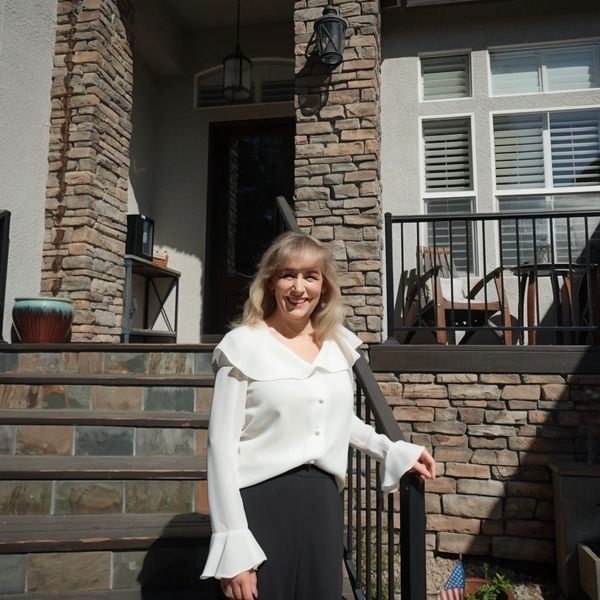 Woman standing on stairs in front of a stone house, smiling.