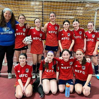 Girls' indoor soccer team posing with coach in front of goal net.