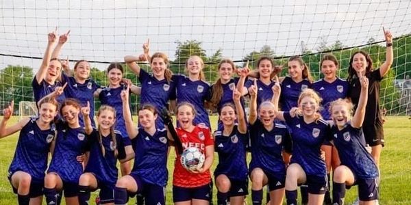 A joyful girls' soccer team posing in front of the goal net, celebrating.