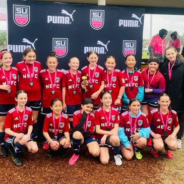 Youth soccer team in red jerseys posing with medals at a Puma-sponsored event.