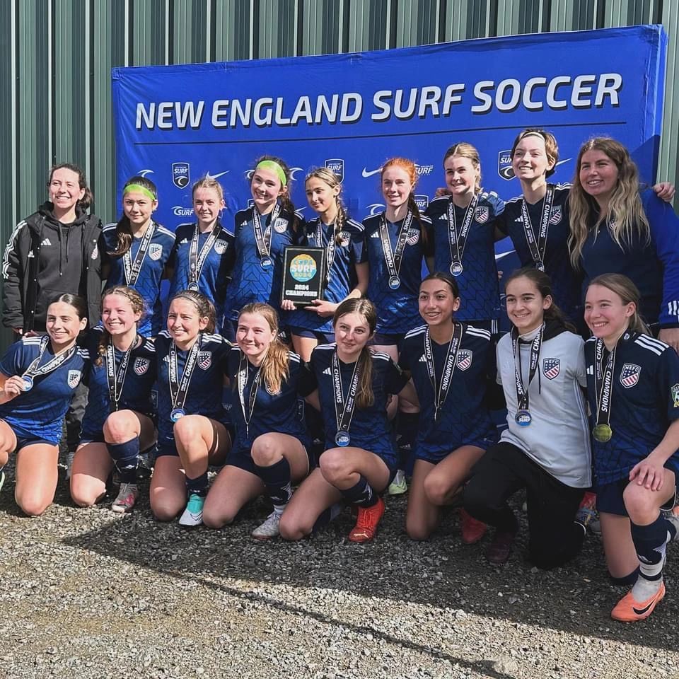 Girls' soccer team posing with medals and a championship plaque.