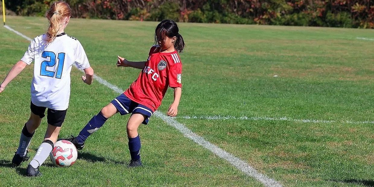 Two girls competing for the soccer ball on a sunny field.