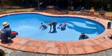 Workers cleaning an empty swimming pool under the sun.