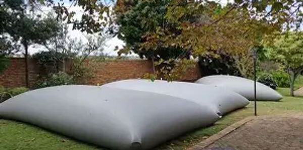 Large grey inflatable cushions placed on a grassy lawn near a brick wall.