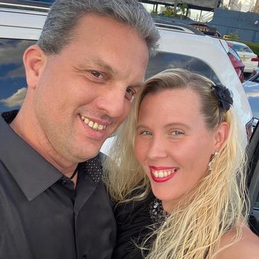 A smiling couple posing outdoors beside a car.