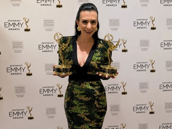Woman proudly holding two Southeast Emmy Awards in a green and black dress.