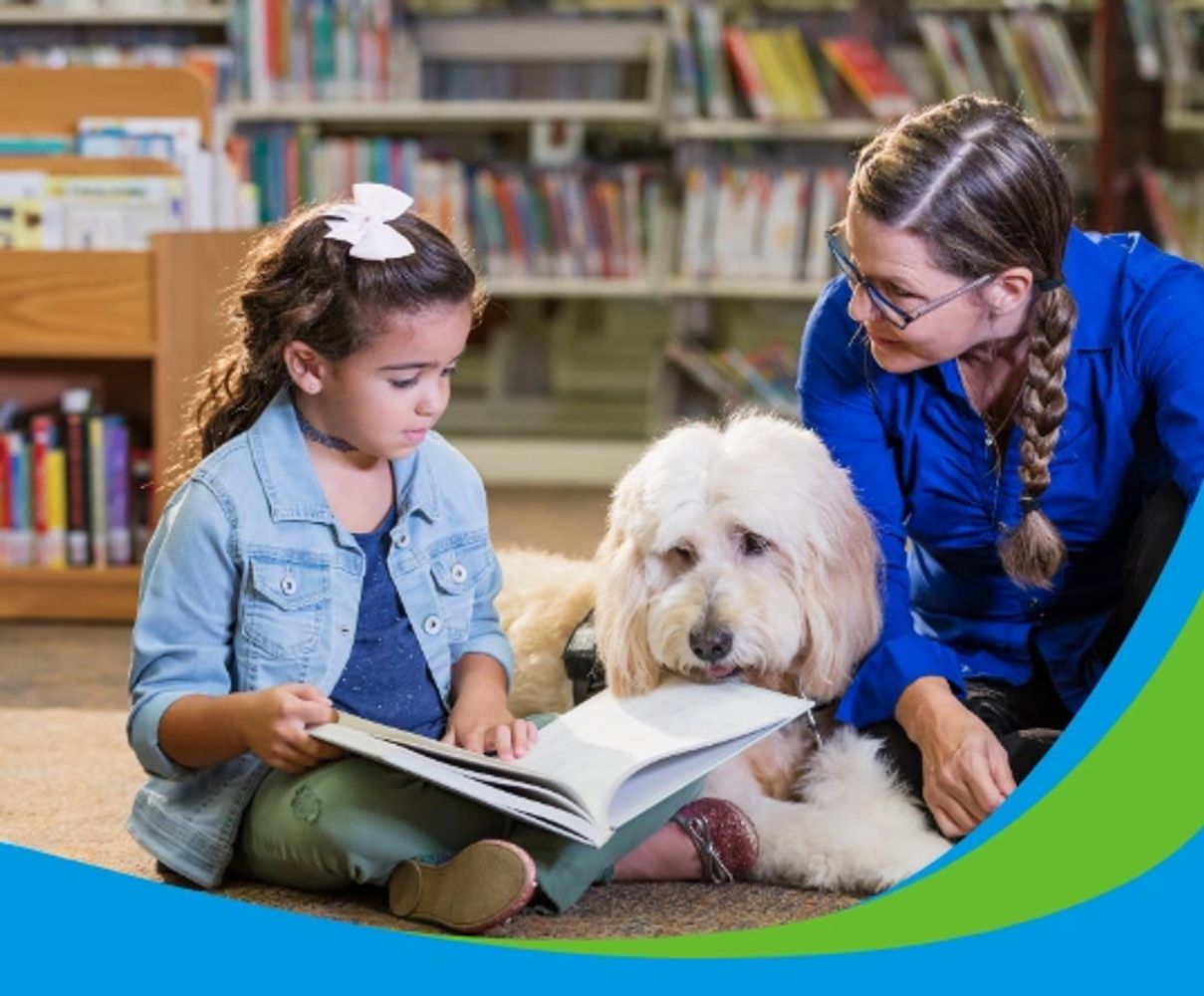 Girl and woman reading book to a therapy dog.
