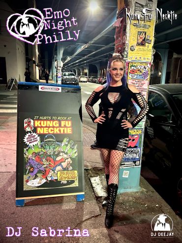 Woman in black emo outfit poses next to Kung Fu Necktie sign at night in Philly.