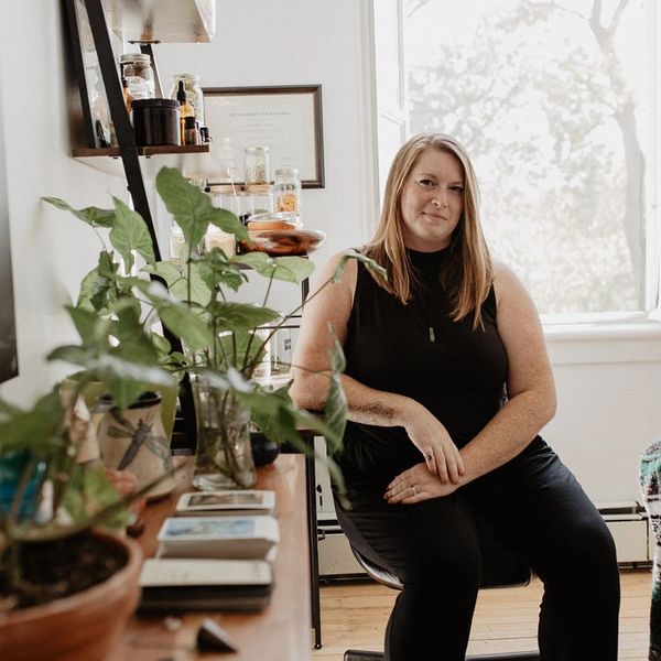 Woman sitting in a cozy, plant-filled room with natural light.