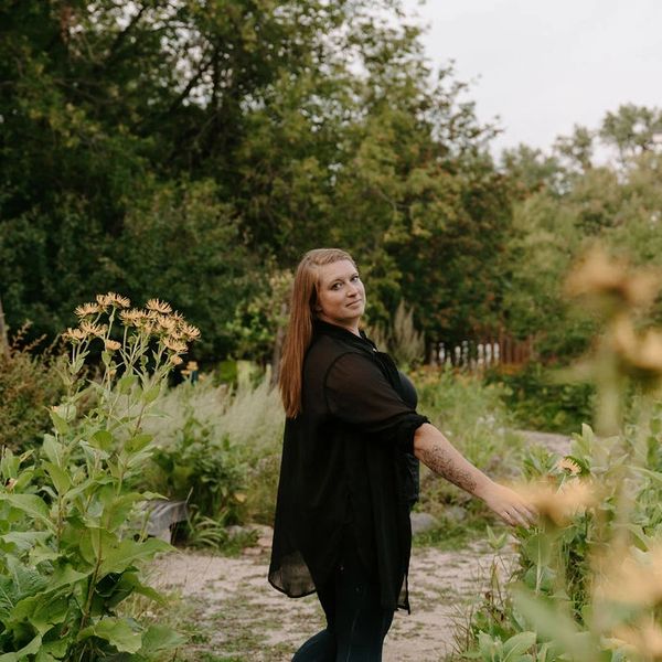 Woman in black shirt walking in a lush garden path, looking back.
