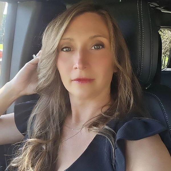 Woman with long hair sitting in a car, posing for a selfie.