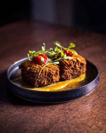 Two crispy fried food pieces garnished with herbs and sauce on a black plate.