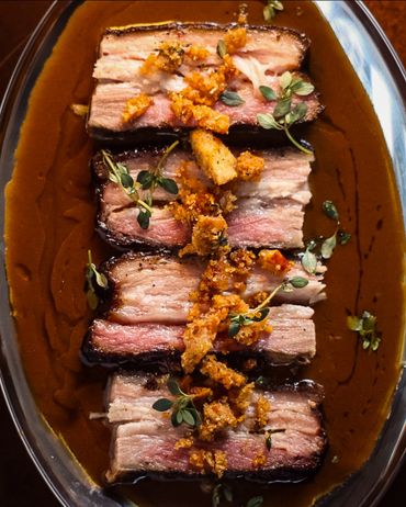 Sliced steak with herbs and crispy garnish on rich sauce.