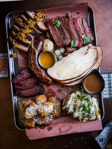 A tray filled with various smoked and grilled meats alongside sides and sauces.