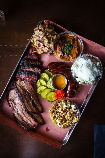 A platter of smoked meats with sides including pickles and beans.