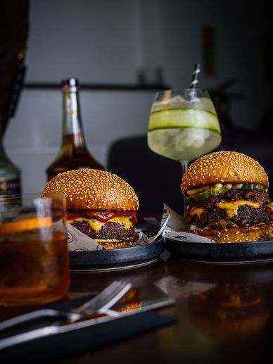Two juicy cheeseburgers with sesame buns and drinks on a table.