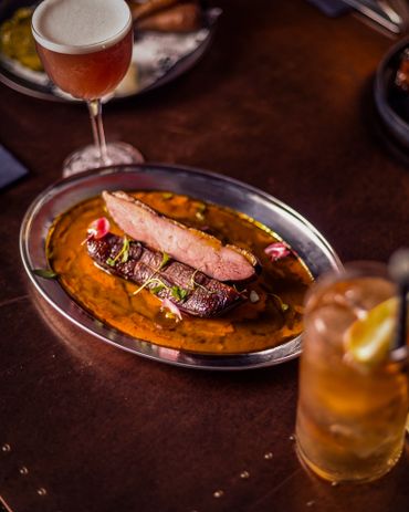 Gourmet meat dish with sauce and two cocktails on a rustic table.